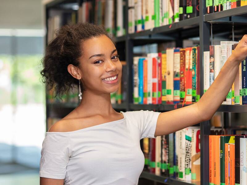 Schülerin in der Bibliothek greift nach einem Buch