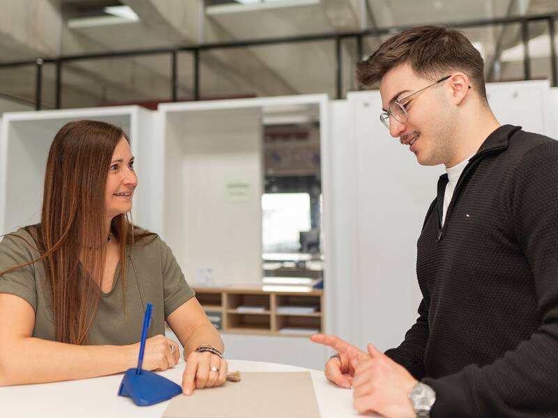 Ein Mann und eine Frau unterhalten sich lächelnd an einem Tisch in einem Büro.