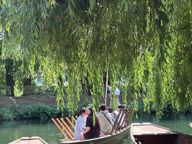 Eine kleine Gruppe von Menschen sitzt in traditionellen Holzbooten auf einem von hängenden Weiden umgebenen Wasserweg.