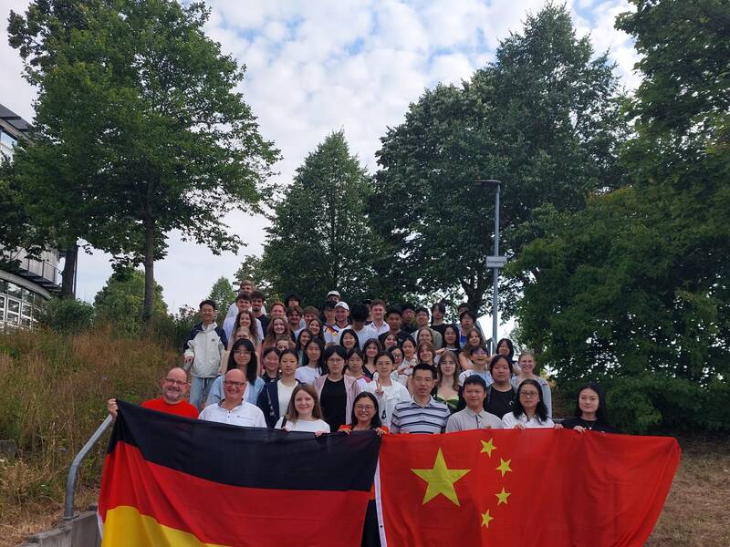 Eine große Gruppe von Menschen steht auf einer Treppe im Freien, während sie die deutsche und die chinesische Flagge hält.