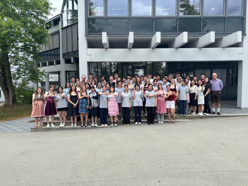 Eine große Gruppe von Menschen steht vor einem modernen Gebäude und posiert lächelnd für ein Gruppenfoto.