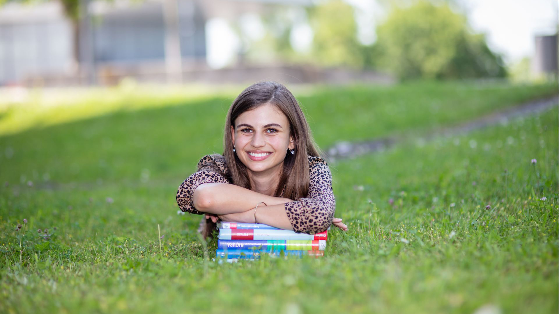 Schülerin liegt auf einem Stapel Bücher im Gras